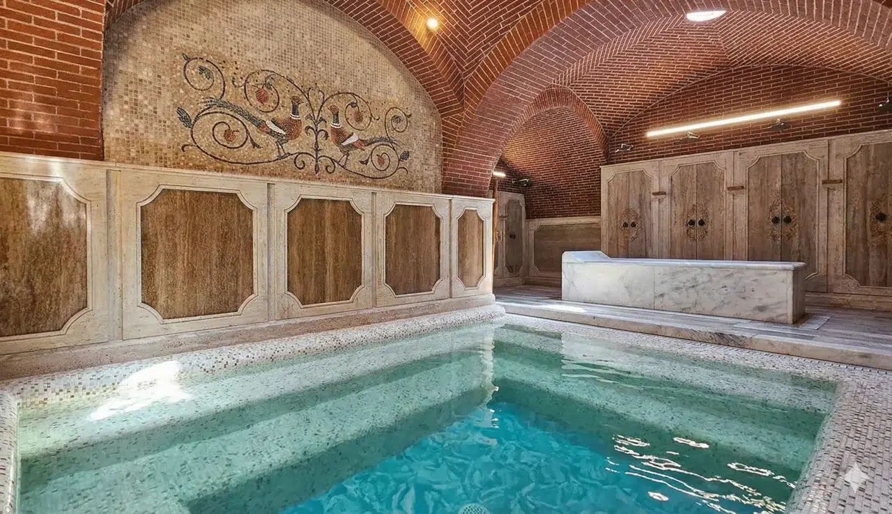 Intérieur d'un bain sulfureux luxueux à Tbilissi, avec un grand bassin d'eau turquoise, une mosaïque murale représentant des paons, des arches en briques rouges, des lambris en bois sculpté et des bancs en marbre.