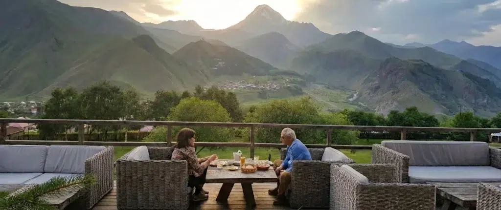 Couple savourant un dîner en terrasse face au mont Kazbek et à l'église de Guerguéti en Géorgie.