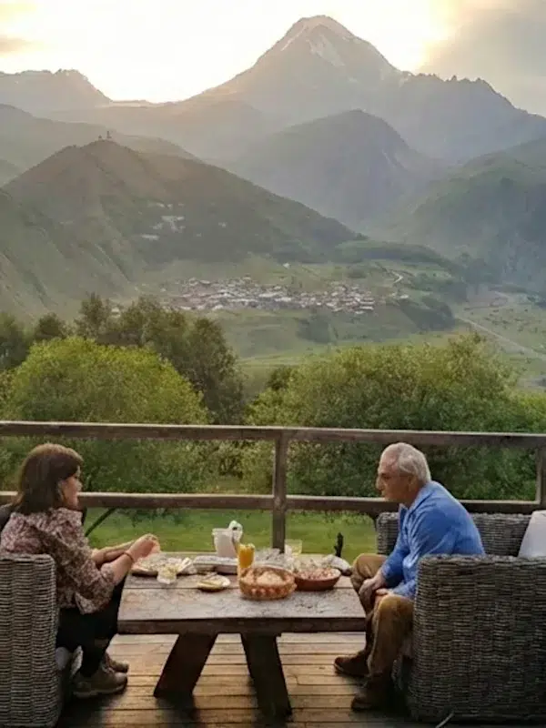 Couple savourant un dîner en terrasse face au mont Kazbek et à l'église de Guerguéti en Géorgie.