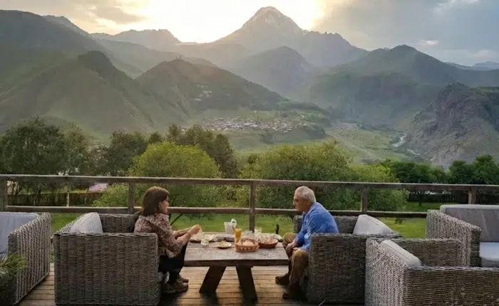Couple savourant un dîner en terrasse face au mont Kazbek et à l'église de Guerguéti en Géorgie.