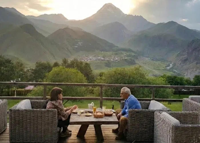 Couple savourant un dîner en terrasse face au mont Kazbek et à l'église de Guerguéti en Géorgie.